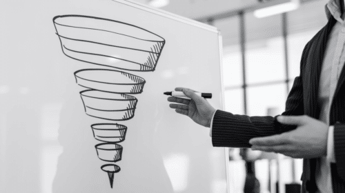 A person in business casual attire presenting a hand-drawn marketing funnel on a whiteboard, gesturing with one hand while holding a marker in the other